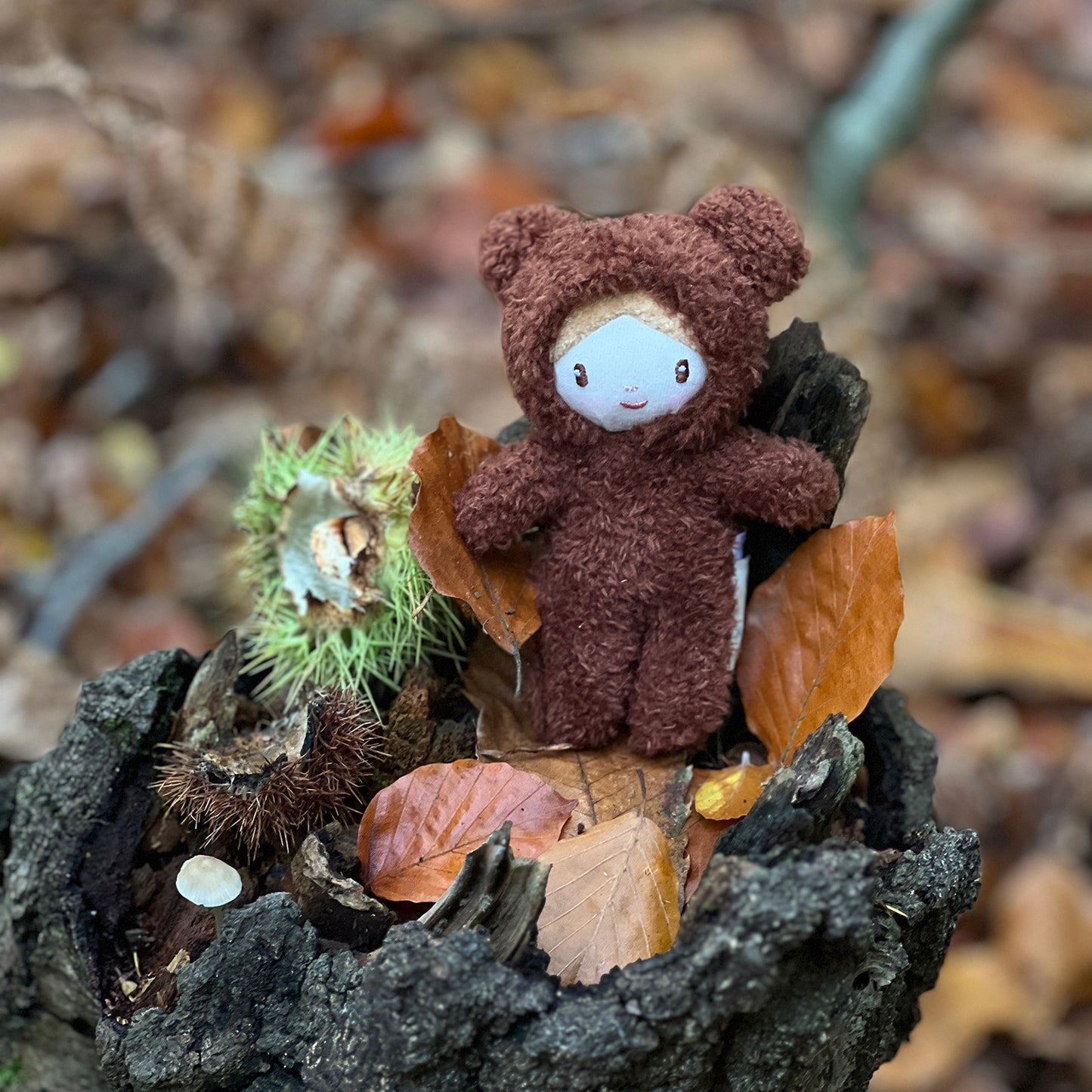 Threadbear Design Heidi Bear Little Peeps Doll in the garden surrounded by leaves.  A pocket size soft toy doll wearing a furry bear suit.  Perfect for dolls houses and imaginative play.